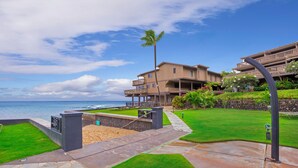 A beachfront property with a well-maintained lawn, a sandy beach area, and a view of the ocean.