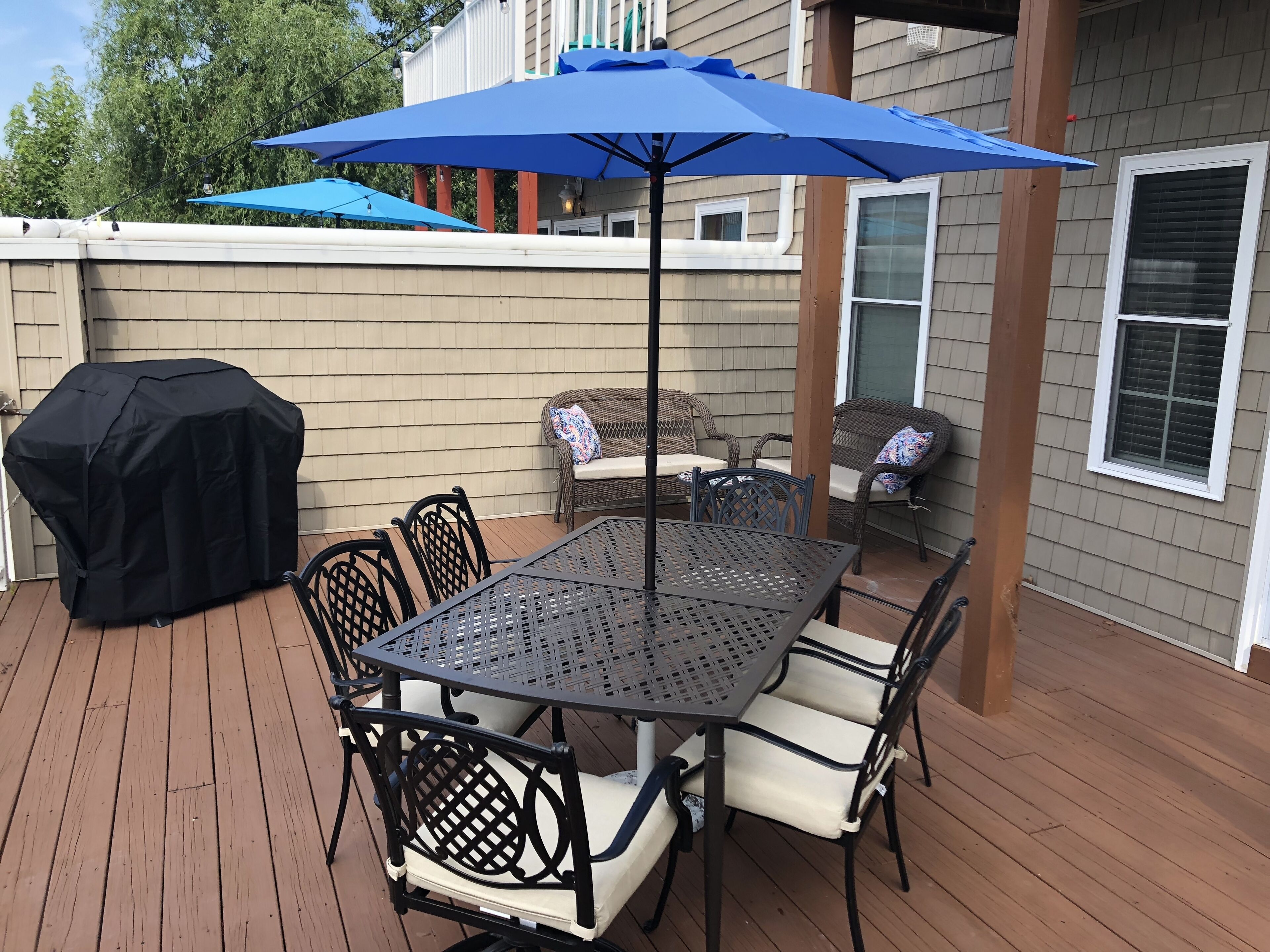 An outdoor patio with a table and chairs, a barbecue grill, and a blue umbrella.
