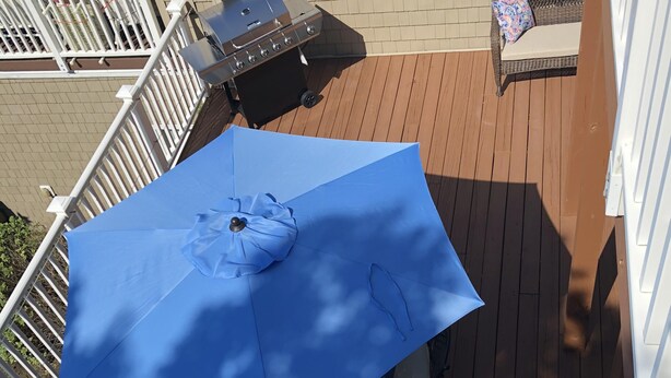 A deck with a blue umbrella, a grill, and outdoor furniture.