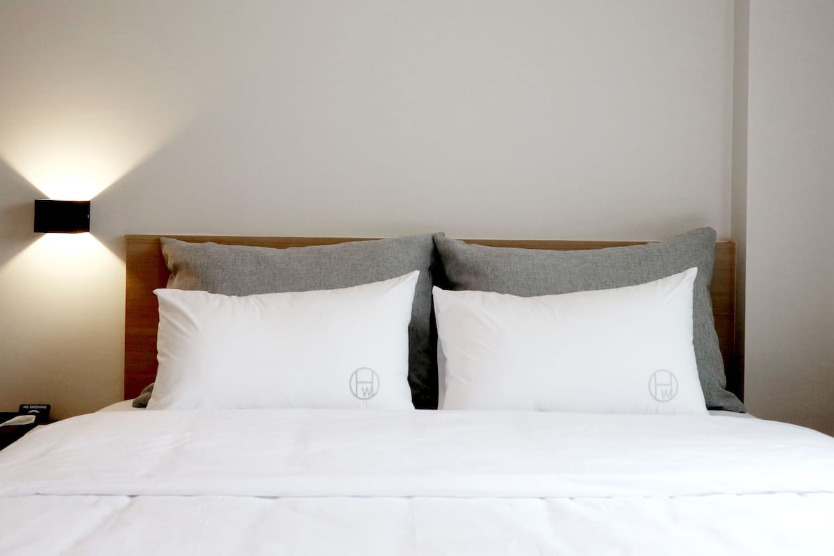 A neatly made bed with white bedding and two pillows, a headboard, and a wall-mounted light fixture.