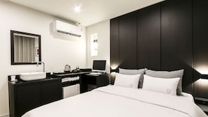 A modern hotel room with a large bed, a bedside table, a built-in desk, a vanity with a mirror, and an air conditioning unit. - The Way Hotel (Busan)