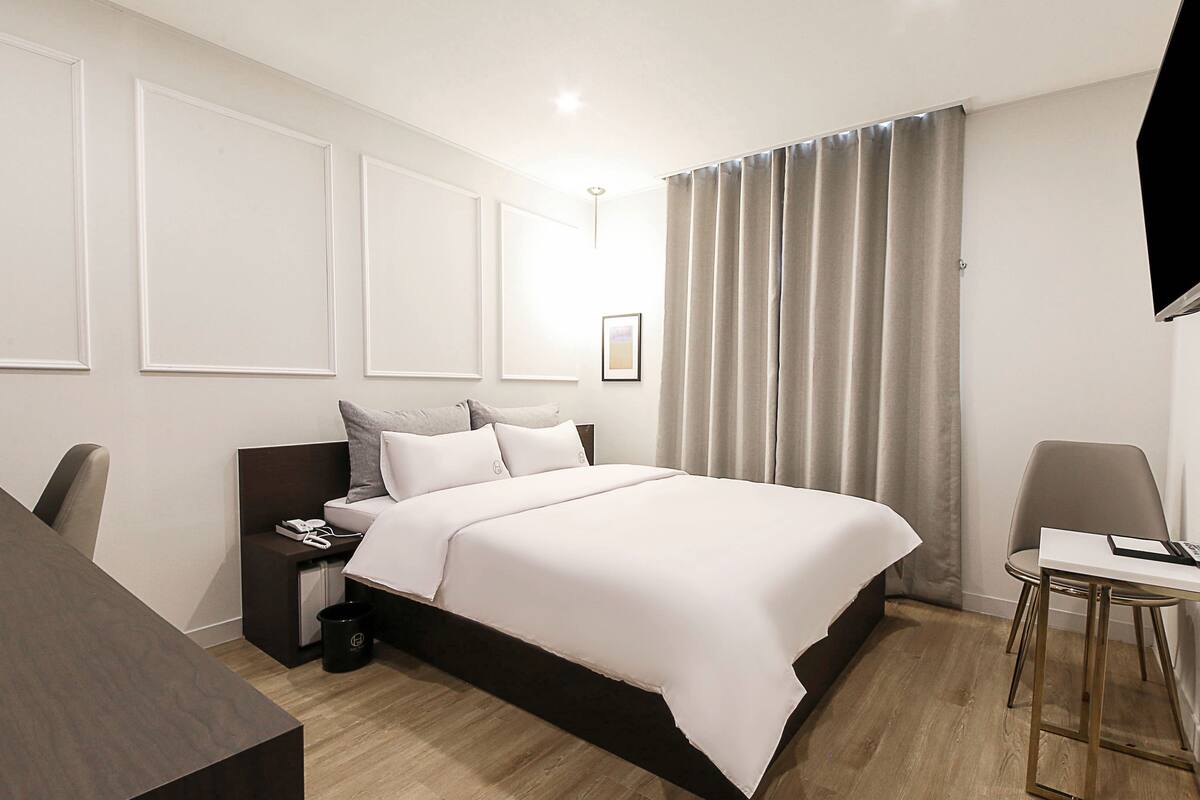 A modern hotel room with a large bed, a desk, and a chair.