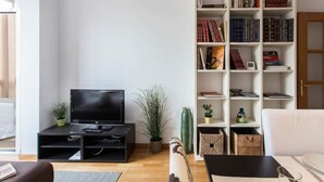 A living room with a black entertainment unit, a flat-screen TV, a bookshelf filled with books, a potted plant, and a white sofa.