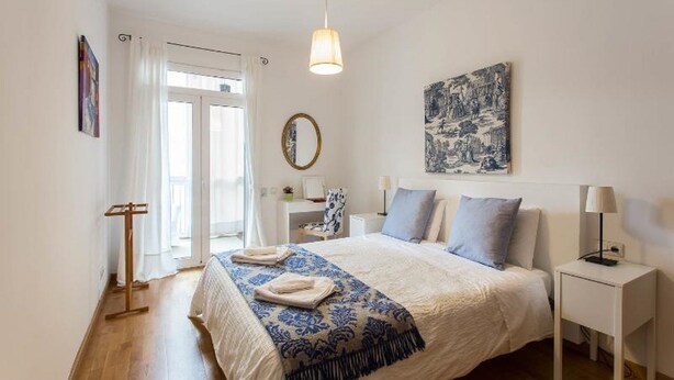 A bedroom with a bed, bedside tables, a desk, a chair, a hanging lamp, a mirror, and artwork on the walls.