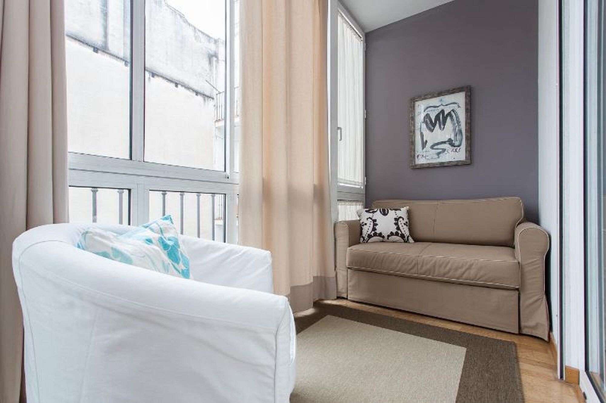 A room with a white armchair, a beige sofa, and a framed abstract artwork on the wall.