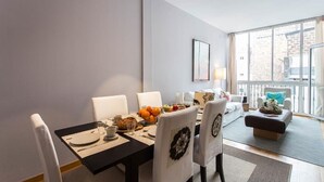 A dining area with a table set for four, chairs with decorative backrests, a fruit bowl, and a window with a view of buildings.