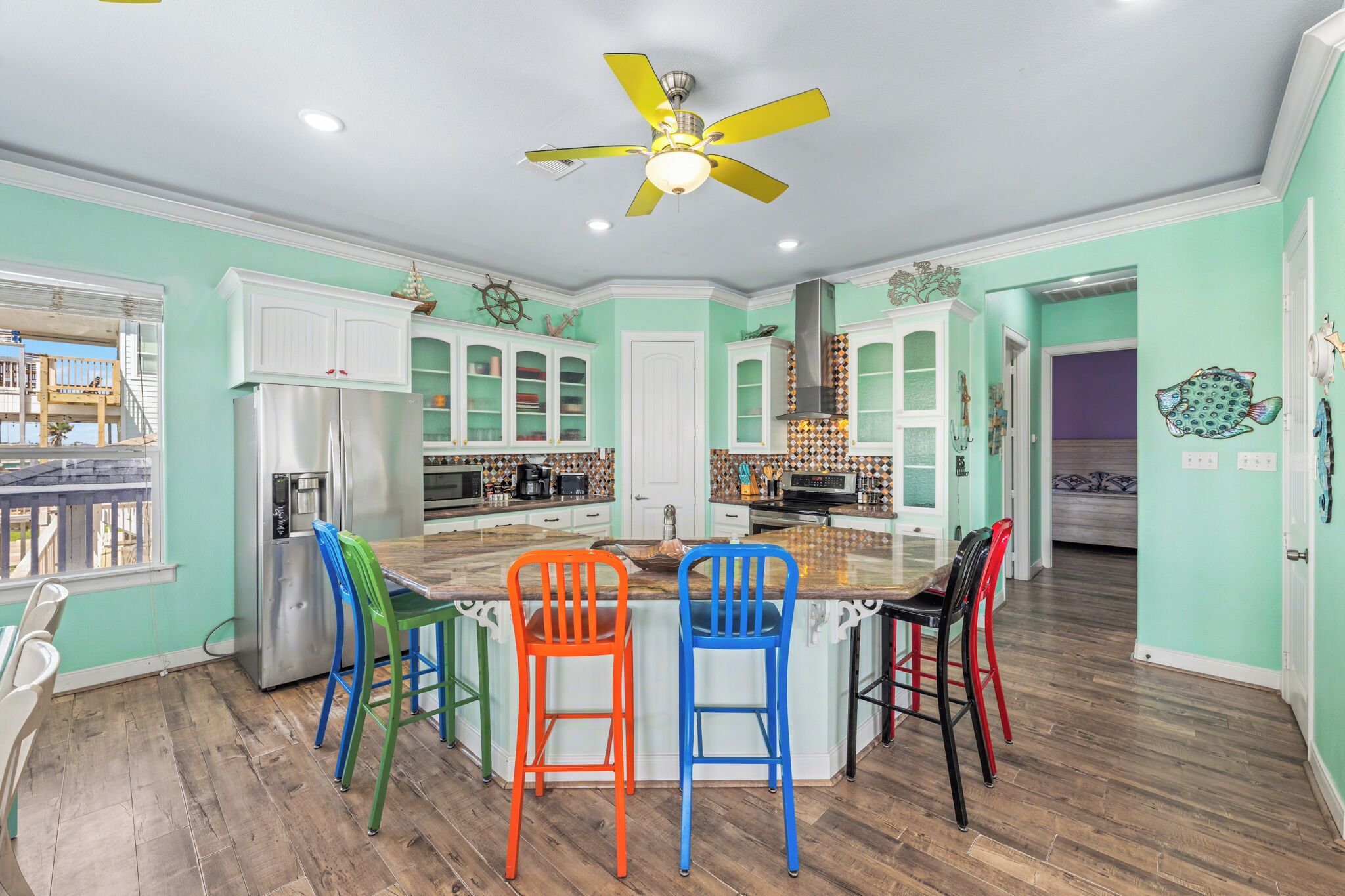 Una cucina con isola centrale, sedie colorate, una ventola a soffitto e vista all'esterno.