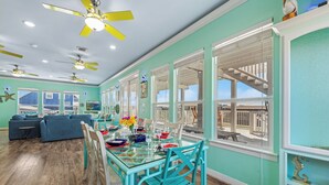 A dining area with a glass table, teal chairs, and ceiling fans.
