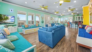 A spacious living area with a large blue sofa, a kitchen area with a bar, and multiple ceiling fans.