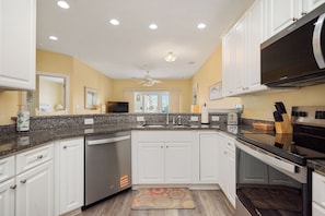 A modern kitchen with white cabinets, granite countertops, stainless steel appliances, and a ceiling fan. - Star Fish: Ocean View Condo with Pool and Hot Tub (Oak Island)