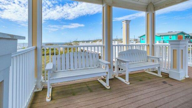 Eine überdachte Veranda mit weißen Geländern und zwei weißen Adirondack-Stühlen.