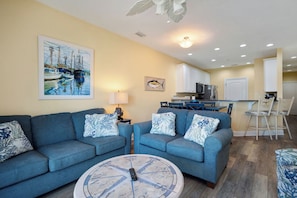 A living room with two sofas, a coffee table, and a painting of boats. - Star Fish: Ocean View Condo with Pool and Hot Tub (Oak Island)