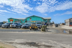 A building with a sign for 'Yaquon Beach Fishing Pier' and a parking area with several vehicles. - Star Fish: Ocean View Condo with Pool and Hot Tub (Oak Island)