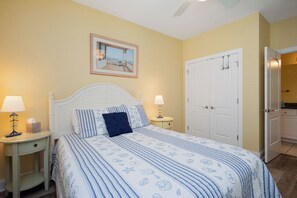 Une chambre à coucher avec un lit, deux tables de chevet, une commode, une porte et un tableau encadré au mur.