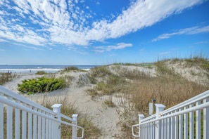A beach view with a white staircase leading down to the sand, a wooden boardwalk, and the ocean in the distance. - Star Fish: Ocean View Condo with Pool and Hot Tub (Oak Island)