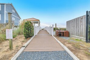 A wooden pathway leading to a covered structure with a metal roof, flanked by a wooden fence and a building with a 'PRIVATE ACCESS' sign. - Star Fish: Ocean View Condo with Pool and Hot Tub (Oak Island)