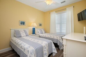 Une chambre avec deux lits, une table de chevet avec une lampe, une télévision et une fenêtre avec des stores.