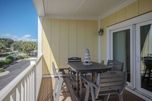 A balcony with a table and chairs, a decorative lighthouse, and a view of the street and greenery. - Star Fish: Ocean View Condo with Pool and Hot Tub (Oak Island)