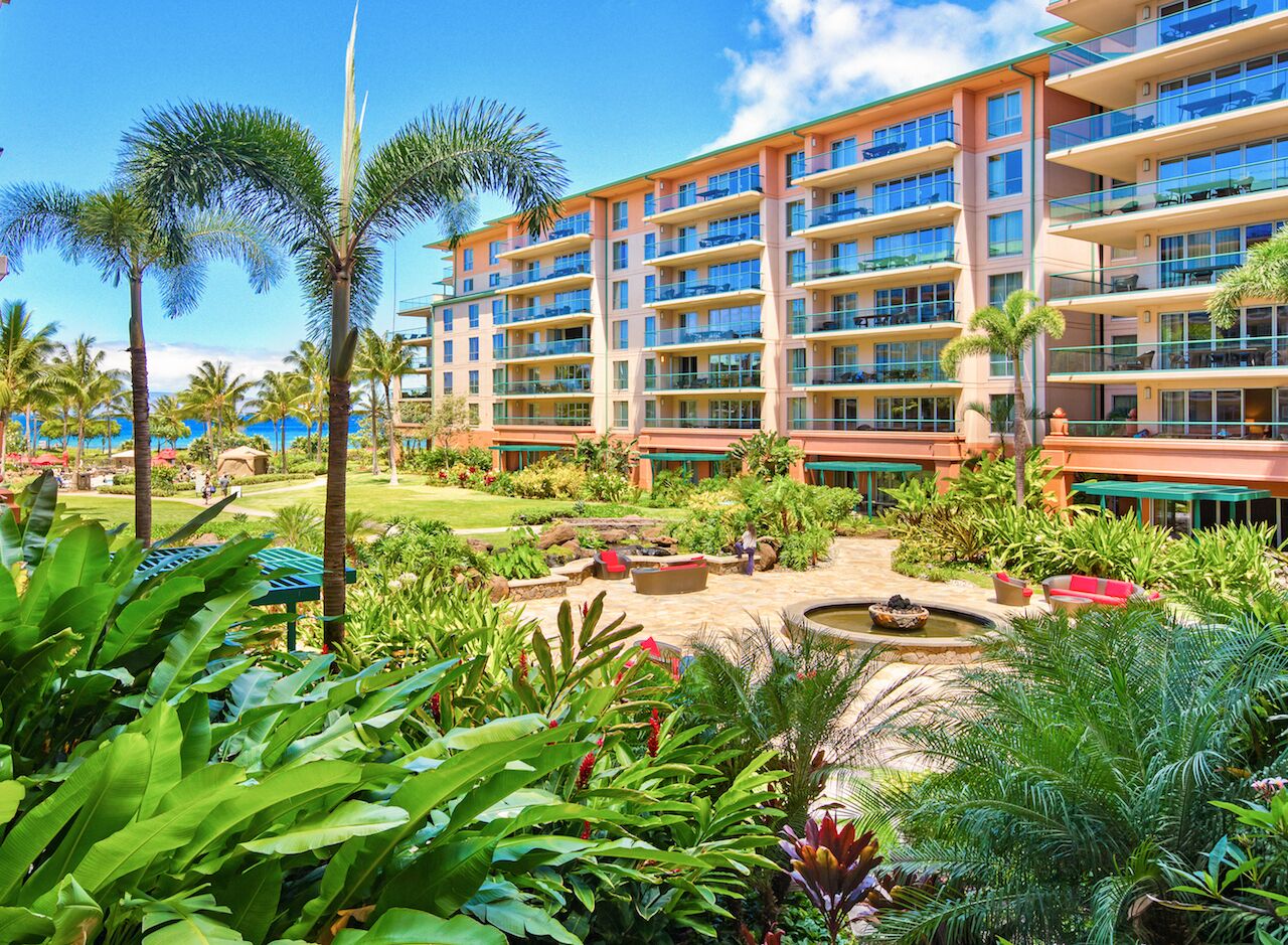 A hotel with multiple floors, outdoor seating areas, and lush greenery.