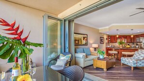 Un soggiorno moderno con una porta vetrata che dà su un balcone, un divano, un tavolino da caffè e una zona cucina visibile attraverso il vetro.