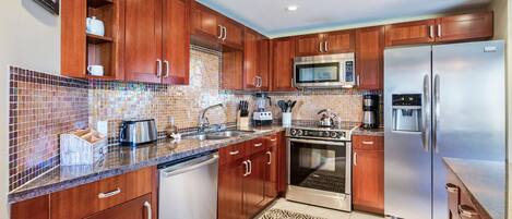 A modern kitchen with wooden cabinets, a stainless steel refrigerator, a microwave, a stove, and a coffee maker.
