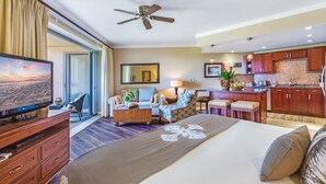 Una camera d'albergo con un letto grande, televisione, ventilatore a soffitto, divano, sedia, scrivania e angolo cottura.