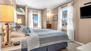 Ein Schlafzimmer mit Bett, Nachttisch, Lampe und einem an der Wand befestigten Fernseher.