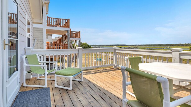 Eine Holzterrasse mit weißer Geländer, grünen Sitzgelegenheiten und einem Tisch.