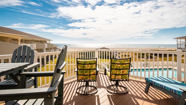 A deck with Adirondack chairs and a pool, overlooking a beach. - Fish Tales: Charming Oceanfront Condo with Wrap-around Deck, Central Location Id (Oak Island)