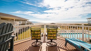 A deck with Adirondack chairs and a pool, overlooking a beach. - Fish Tales: Charming Oceanfront Condo with Wrap-around Deck, Central Location Id (Oak Island)