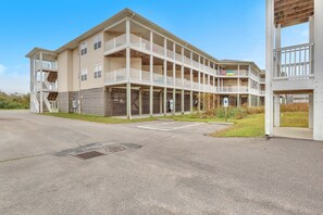 A multi-story building with balconies, a parking lot, and a grassy area.
