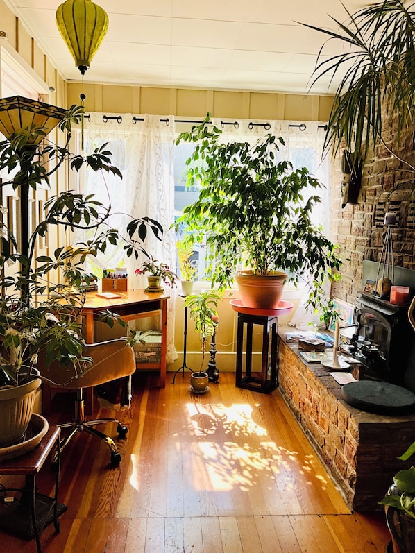 Una habitación con piso de madera, pared de ladrillo, una planta grande en maceta, una mesa y una silla.