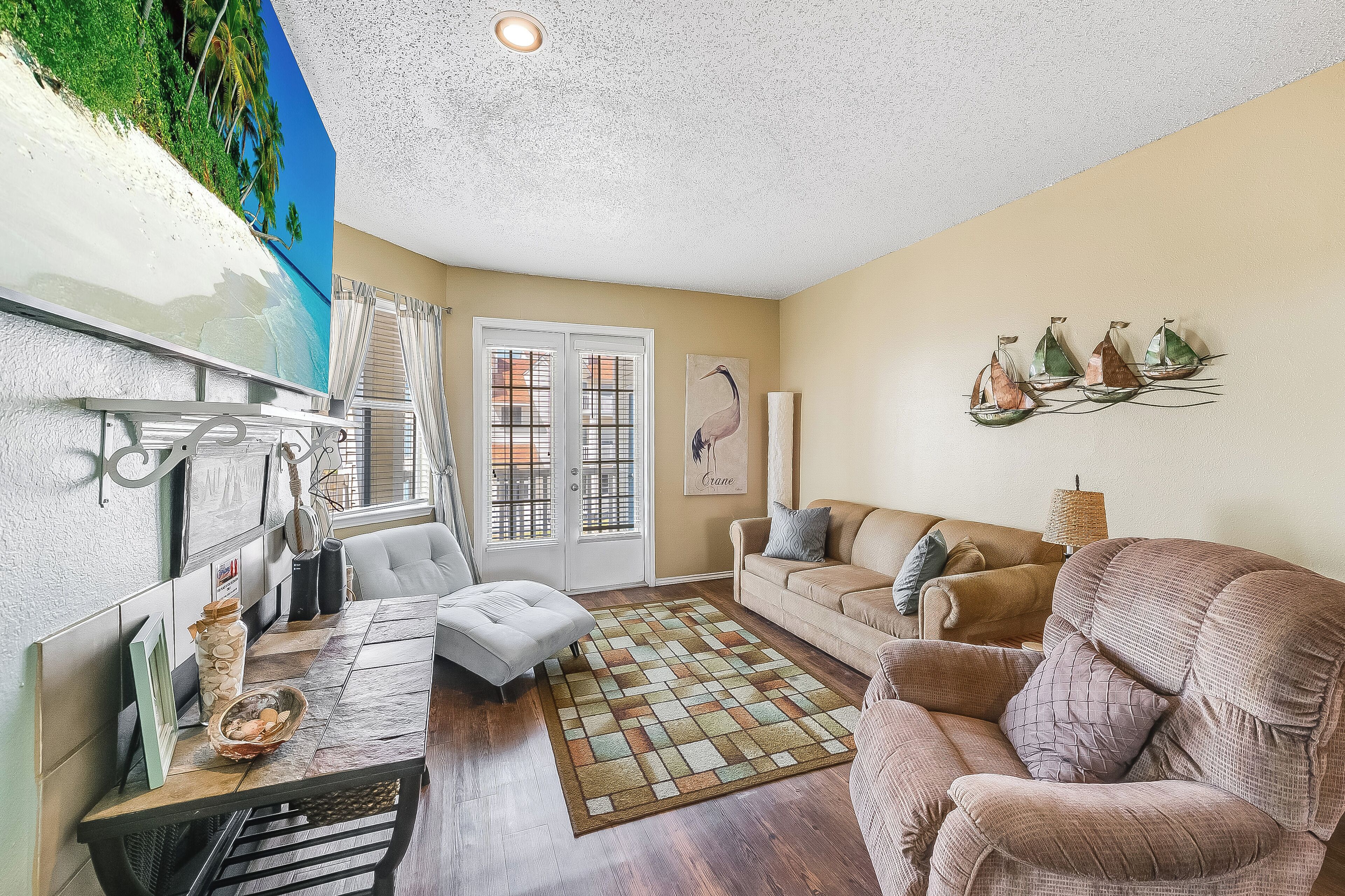 A living room with a large window, a sofa, a coffee table, and a decorative sailboat wall art.