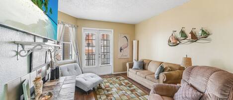 A living room with a large window, a sofa, a coffee table, and a decorative sailboat wall art.