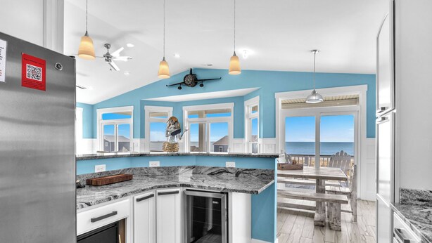 A modern kitchen with a built-in refrigerator, white cabinets, and a granite countertop. There is a view of the ocean through large windows. - Conch Out: Oceanview Home w/Private Pool (Oak Island)