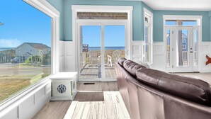 A spacious room with a large window, a brown leather sofa, and a view of the beach. - Conch Out: Oceanview Home w/Private Pool (Oak Island)
