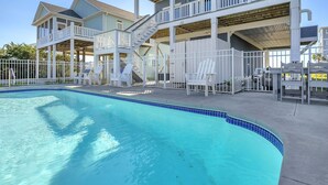A swimming pool with a blue tiled edge, white lounge chairs, and a multi-level building with balconies. - Conch Out: Oceanview Home w/Private Pool (Oak Island)