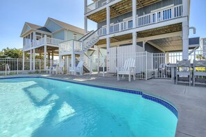 A swimming pool with a blue tiled edge, white lounge chairs, and a multi-level building with balconies. - Conch Out: Oceanview Home w/Private Pool (Oak Island)