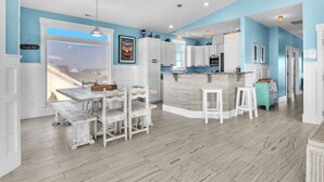 A modern kitchen with white cabinets, a marble island, and a view to the outside. - Conch Out: Oceanview Home w/Private Pool (Oak Island)