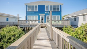 Une promenade en bois mène à un bâtiment à deux étages dont la façade est bleue et les ornements blancs.
