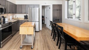 Une cuisine moderne dotée d’appareils électroménagers en acier inoxydable, d’une table à manger en bois et offrant une vue sur l’extérieur grâce à de grandes fenêtres.