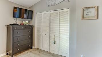 A room with a dark wooden dresser, a television, a white closet with louvered doors, and a wall-mounted fish decoration.