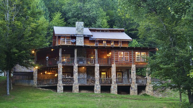 A large, multi-story log cabin with a stone chimney, multiple balconies, and a well-maintained lawn.