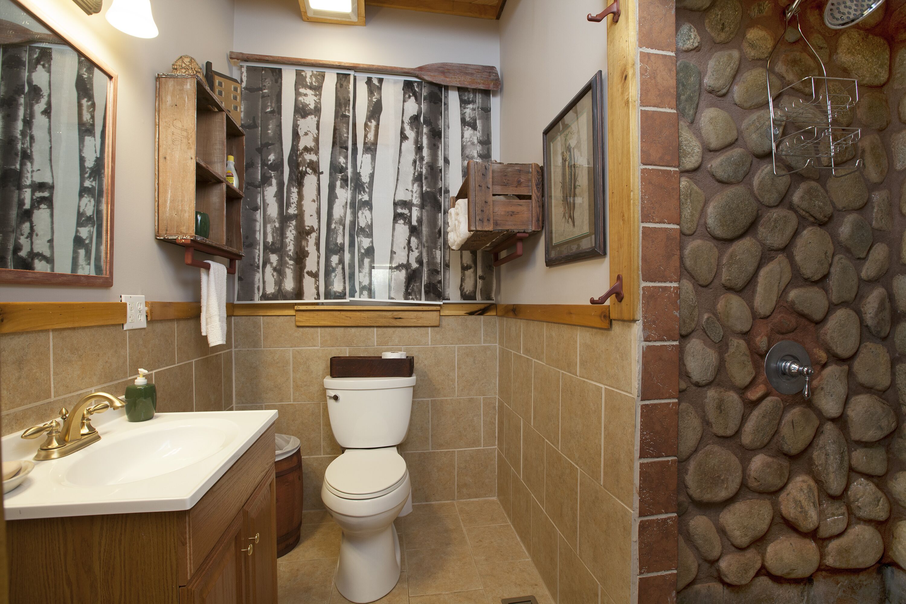 Un baño con inodoro blanco, tocador de madera y pared de ducha de piedra.