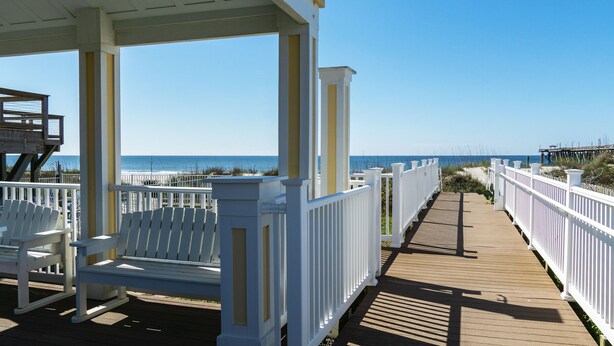 A wooden boardwalk with white railings and benches, leading to a beach.
