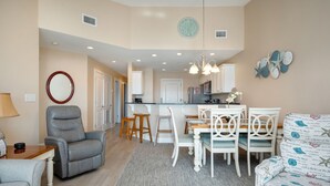 A living room with a grey recliner, a dining table with white chairs, and a patterned sofa.
