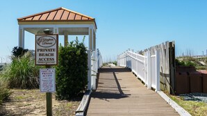 A wooden boardwalk leading to a gazebo with a beach access sign.