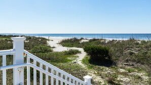A coastal pathway leading to a beach with a white railing in the foreground.
