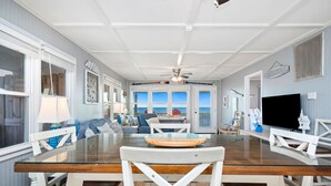 A spacious dining area with a glass-top table, white chairs, and a ceiling fan. - Sandy Dunes: Spectacular Oceanfront Home with Amazing Views (Oak Island)
