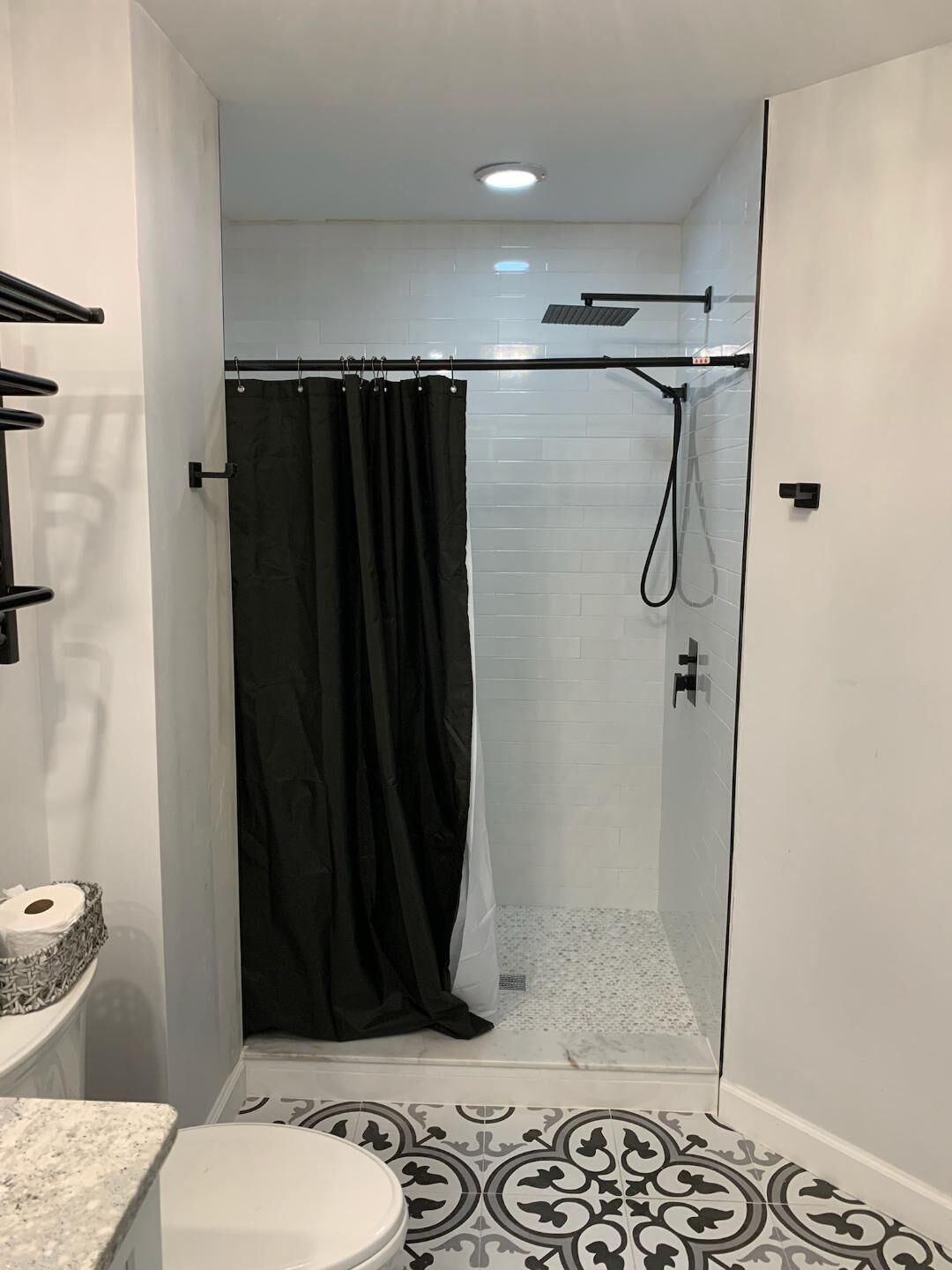 Une salle de bain moderne avec une douche à parois de verre, un rideau de douche noir, des toilettes et des carreaux de sol à motifs.